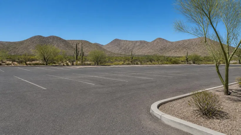 Commercial parking lot in the Sonoran desert with white stall lines, a curbed landscaping island and bare desert ridges beyond
