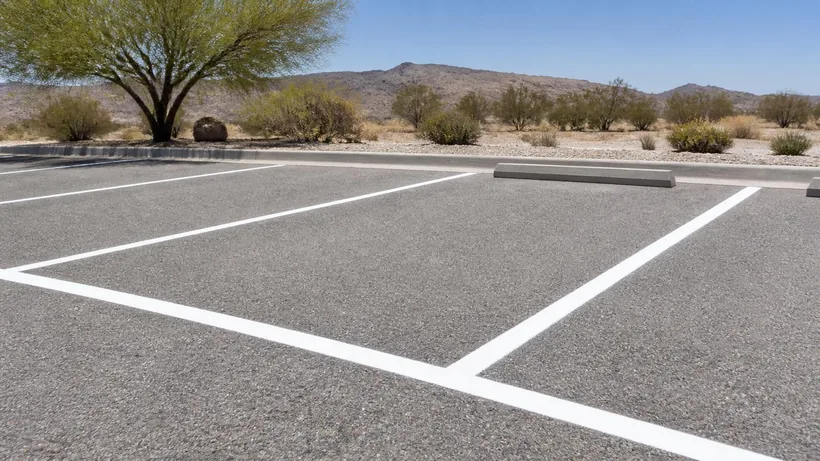 Freshly painted white stall lines and a concrete wheel stop on sun-bleached asphalt in a desert lot