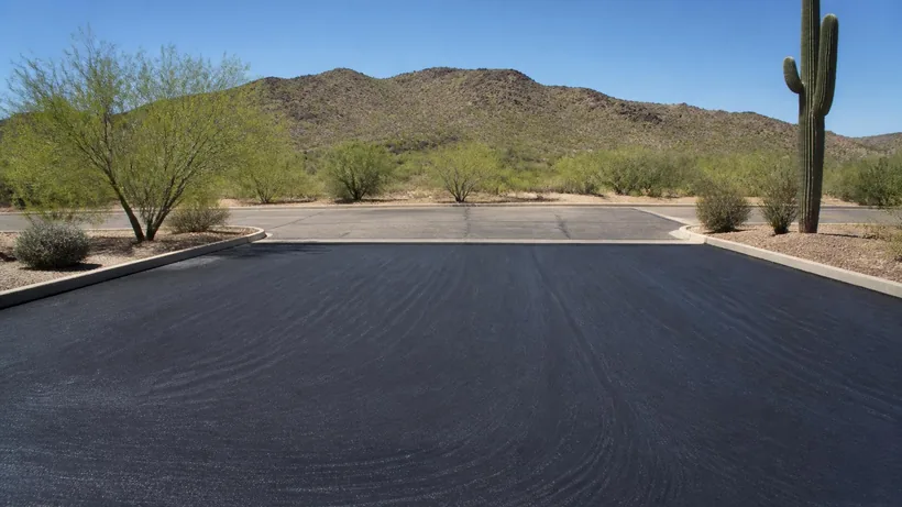 Uniform satin black sealcoat across a desert parking lot with squeegee arcs still visible in the coating
